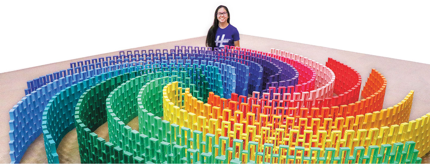 Lily Hevesh poses and smiles with her display made out of thousands of multicolored dominoes.